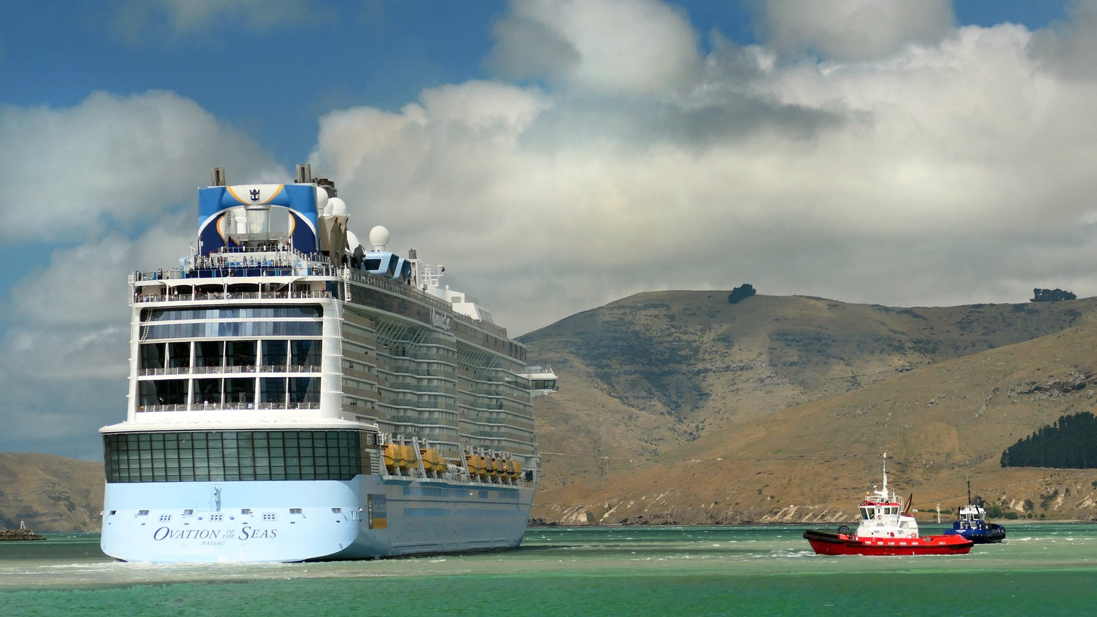 Royal Caribbean Ovation of the Seas cruise ship at sea near tugboats, stern view