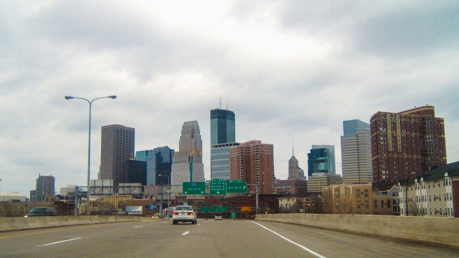 The driver's view of eastbound Interstate 394 entering downtown Minneapolis, with the skyline ahead and green overhead signs for the 4th Street North and 12th Street North exits