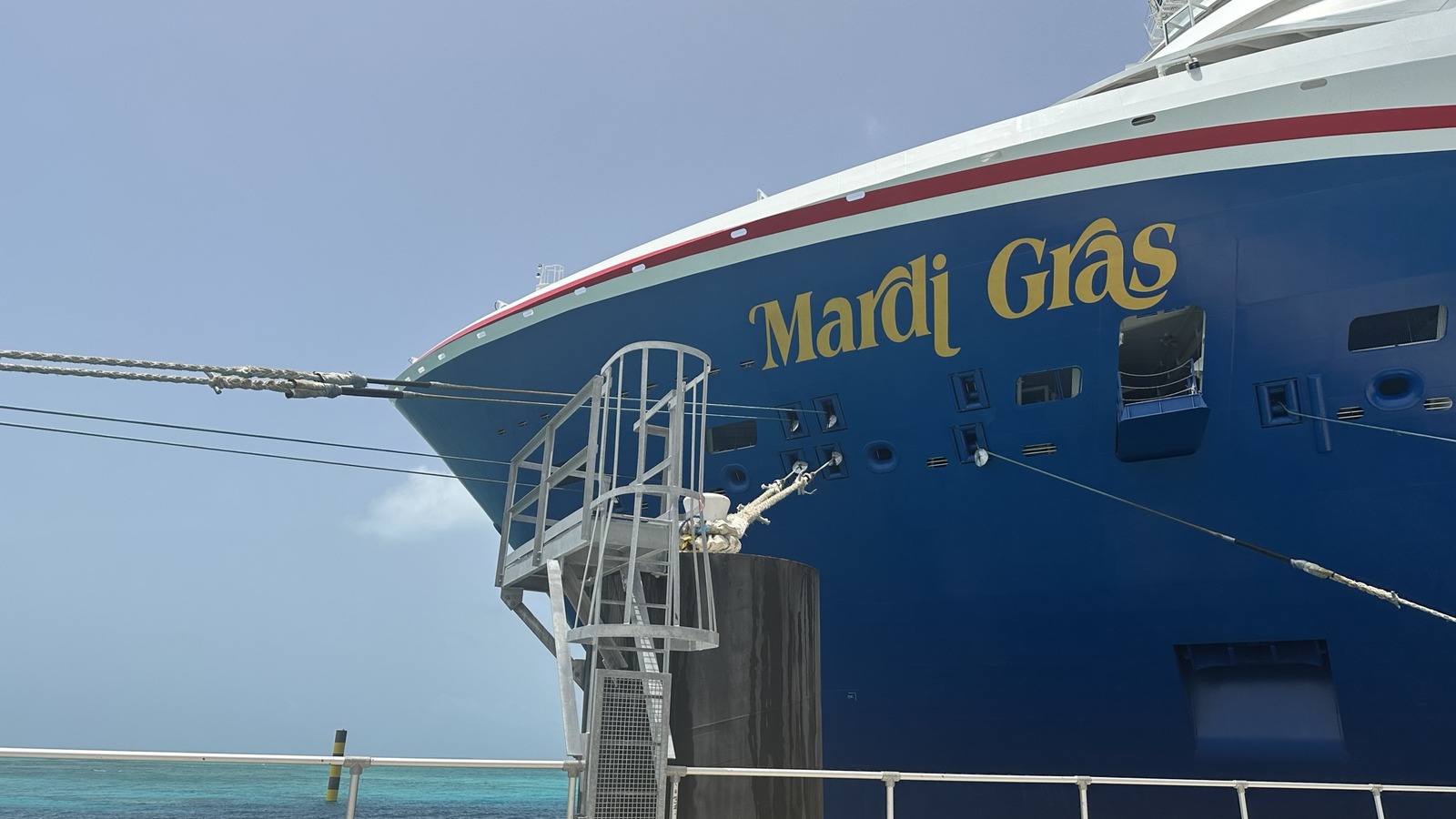 Carnival Cruise Line ship Mardi Gras docked at a bright Caribbean pier, with the gold Mardi Gras name on the blue hull. Image shows the ship, not the credit card.