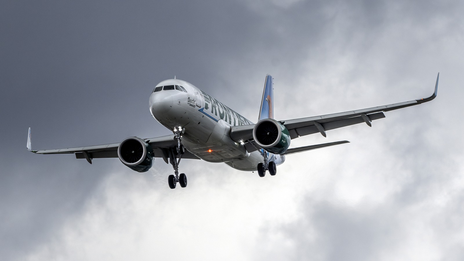 A Frontier Airlines Airbus A320neo on approach under a dark, cloudy sky