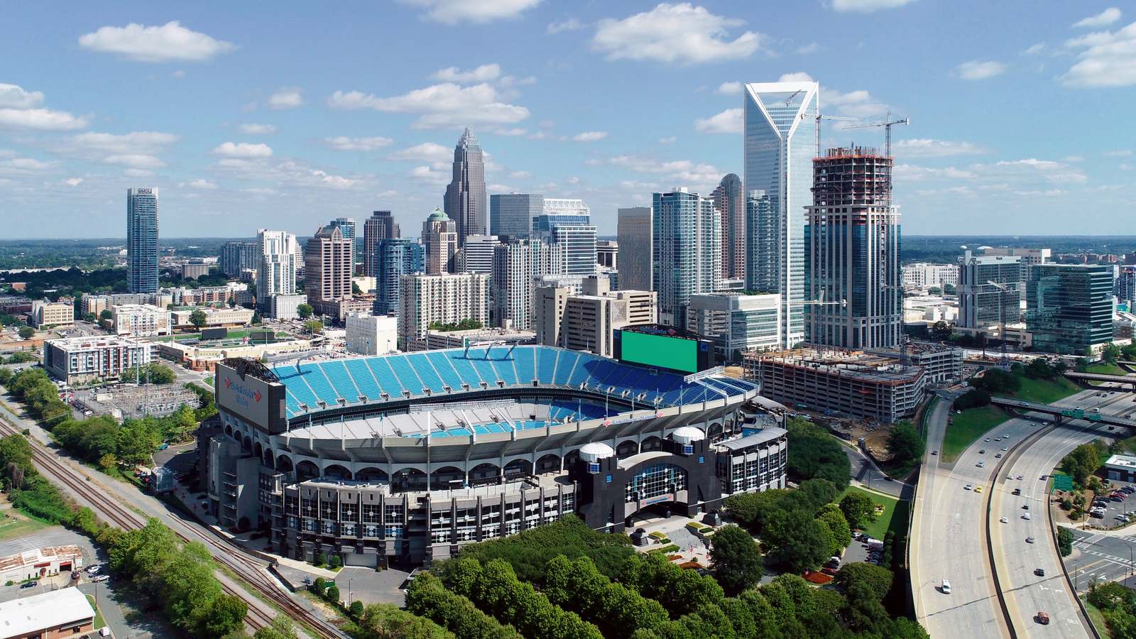 Aerial view of Uptown Charlotte skyscrapers behind Bank of America Stadium, with an interstate curving past on the right.