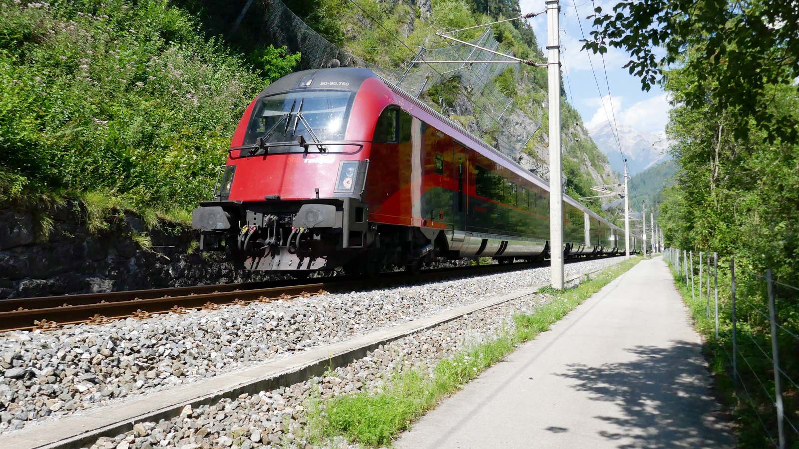 OBB Railjet train running along the Arlberg railway beside a mountain footpath in summer
