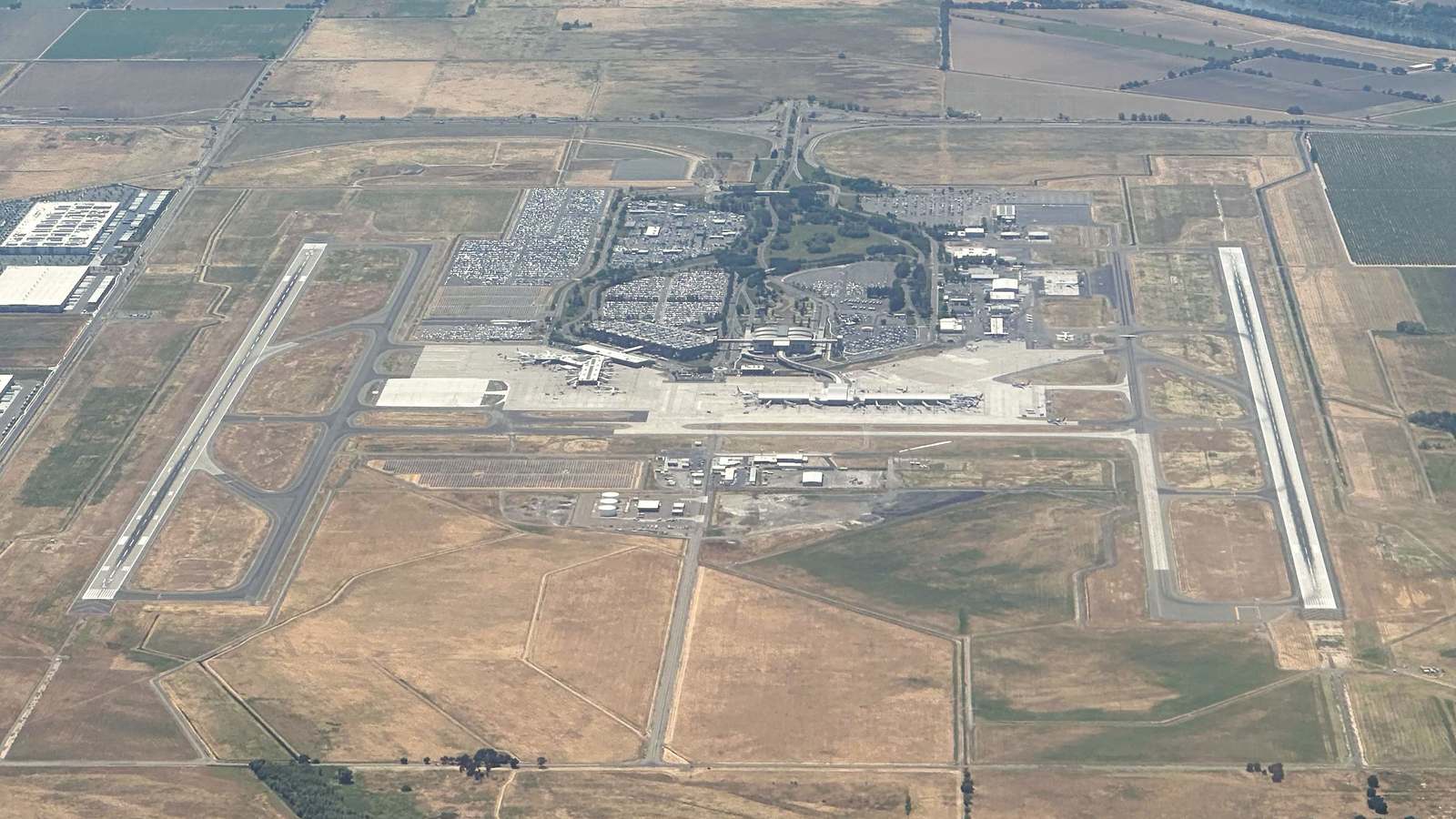 Aerial view of Sacramento International Airport showing both runways, the terminals and surrounding parking lots amid farmland.