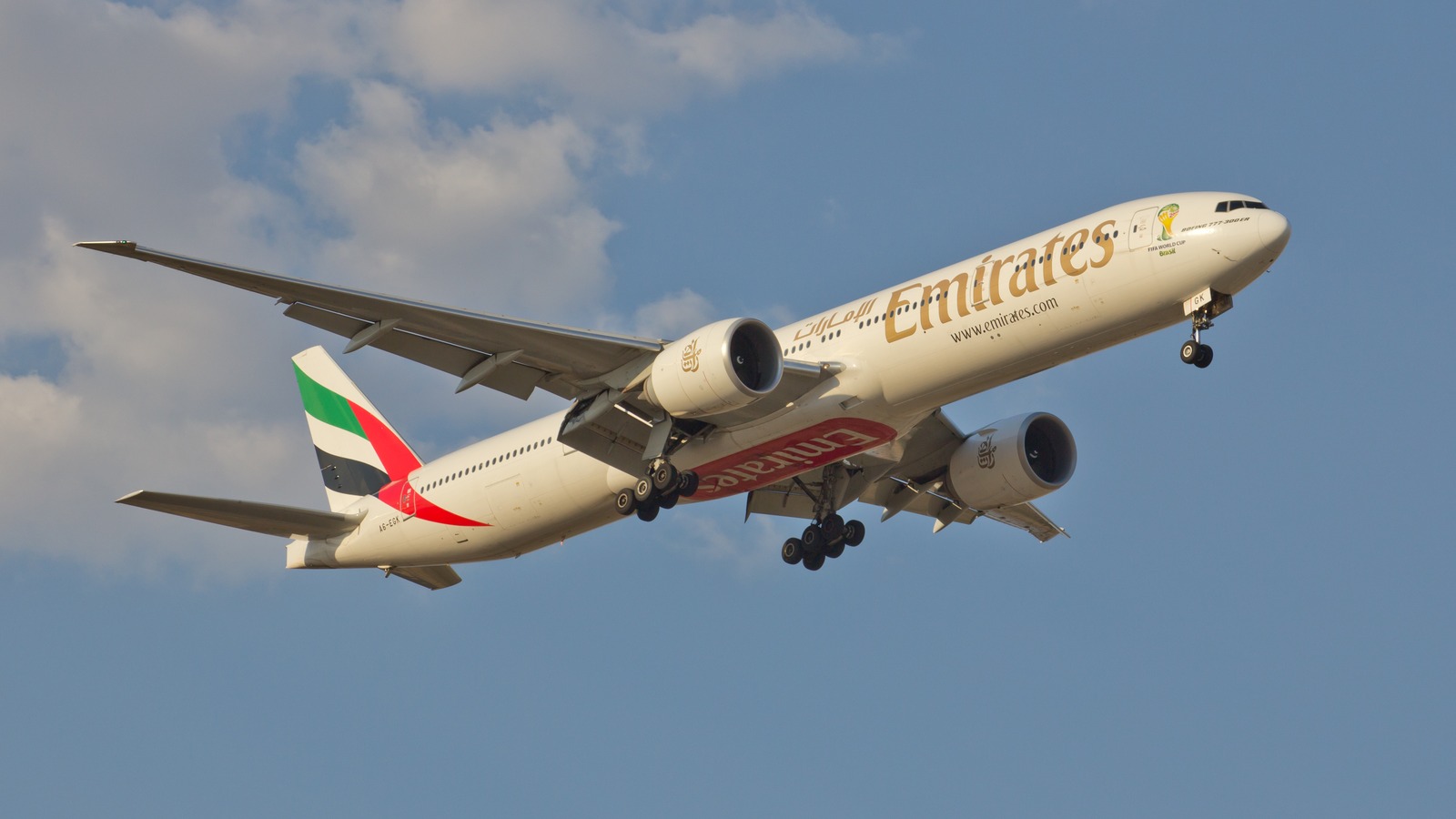Emirates Boeing 777-300ER A6-EGK climbing with landing gear still down against a blue sky
