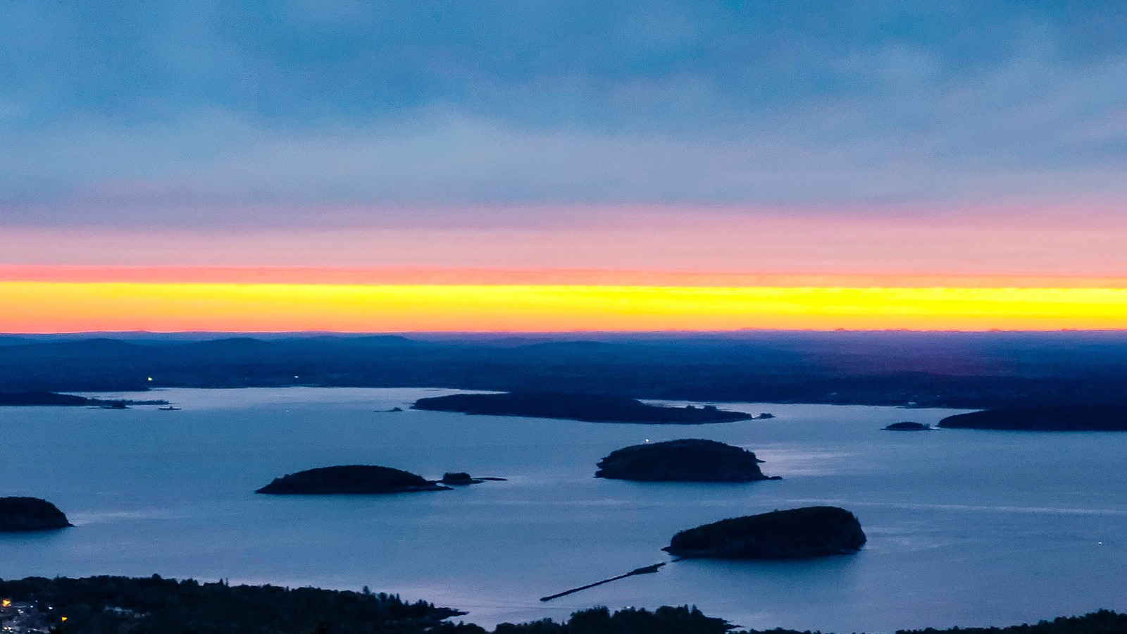 Pre dawn view from the summit of Cadillac Mountain over Frenchman Bay, with the Porcupine Islands in silhouette on still water and an orange band of light along the horizon