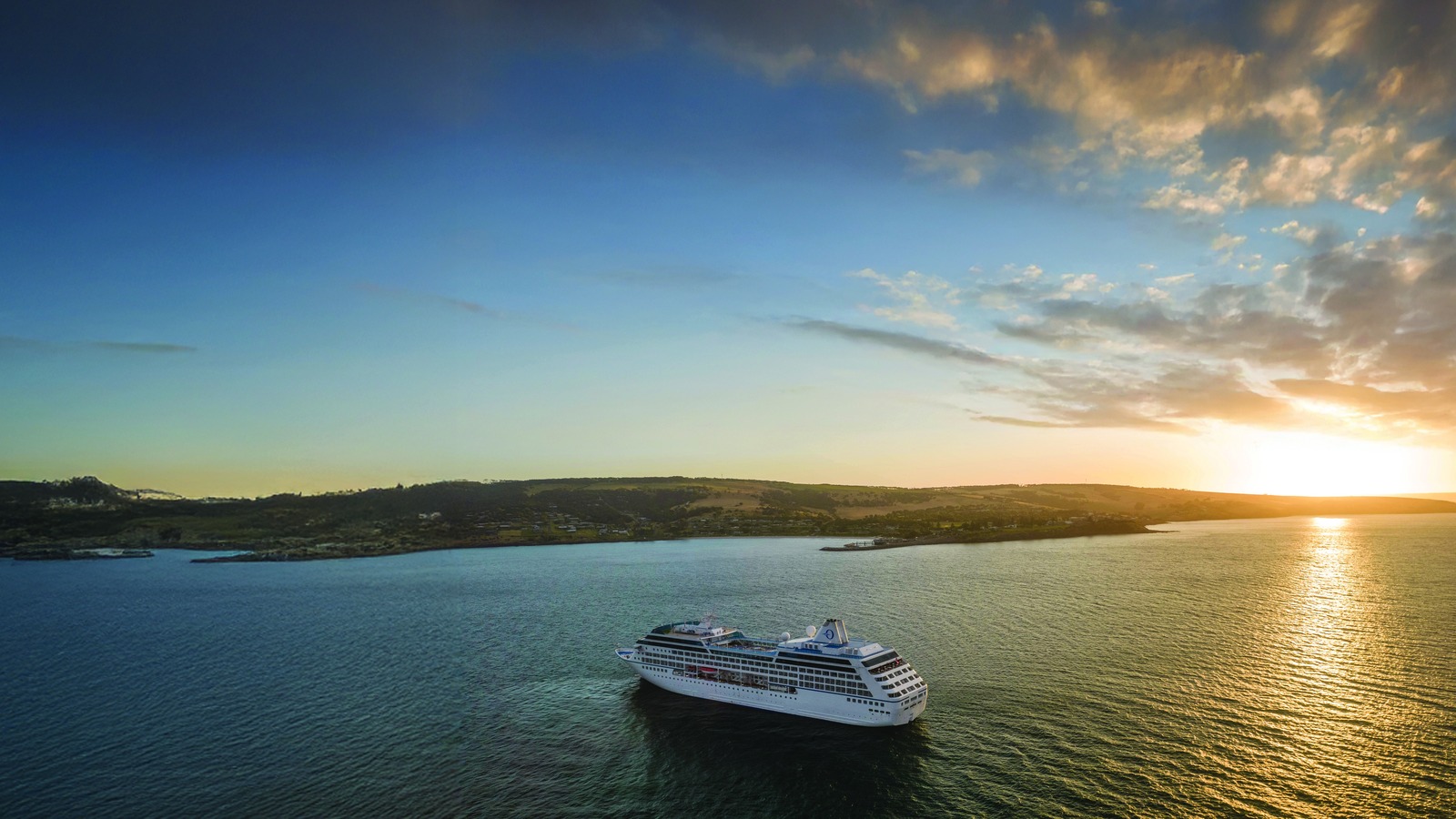 Oceania Aurelia cruise ship at anchor off a coastline at sunset
