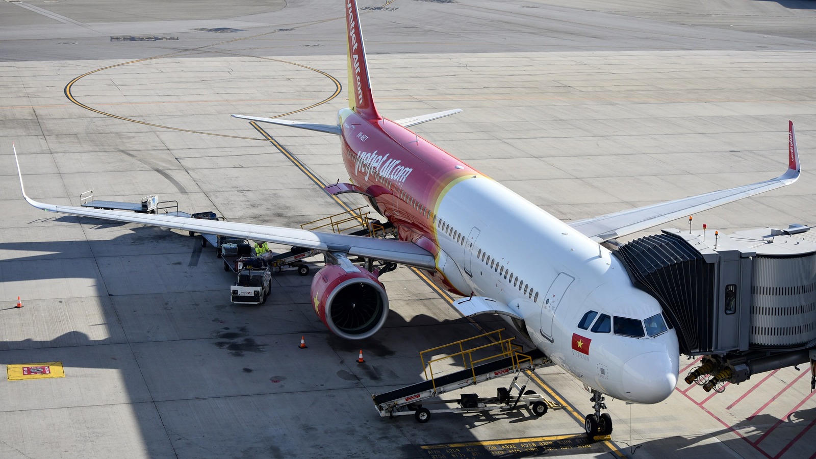 A Vietjet Airbus A321neo in red and white livery parked at an airport gate with a jet bridge attached, seen from above.