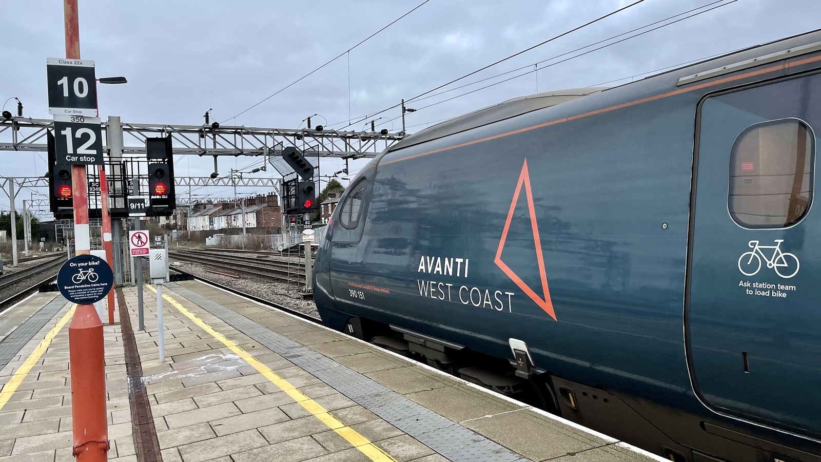 An Avanti West Coast Pendolino, unit 390151, standing at a platform at Stafford railway station under overhead line equipment, with signals and car stop markers on the platform
