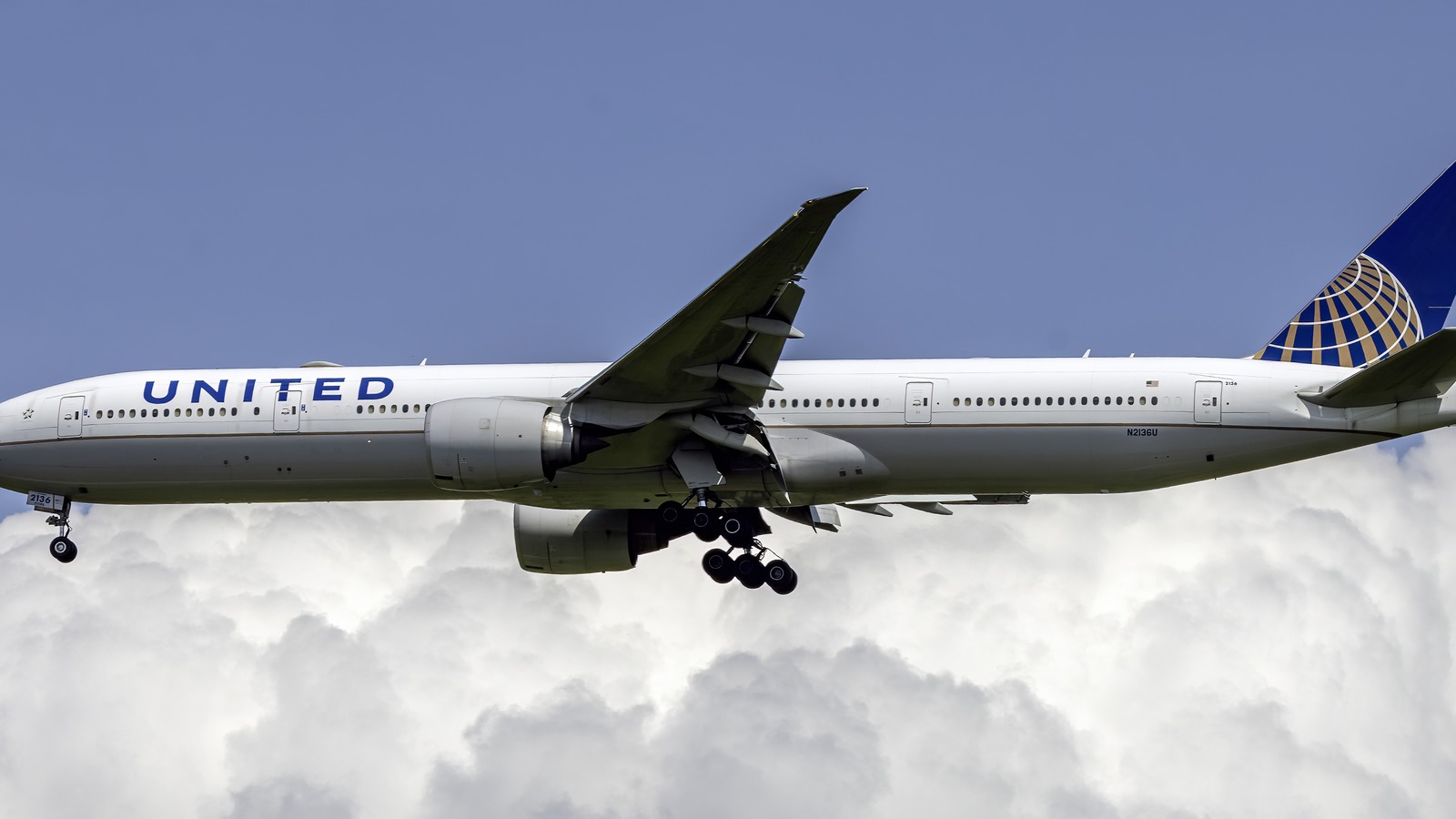 United Airlines Boeing 777-300ER N2136U on approach with landing gear down against a blue sky