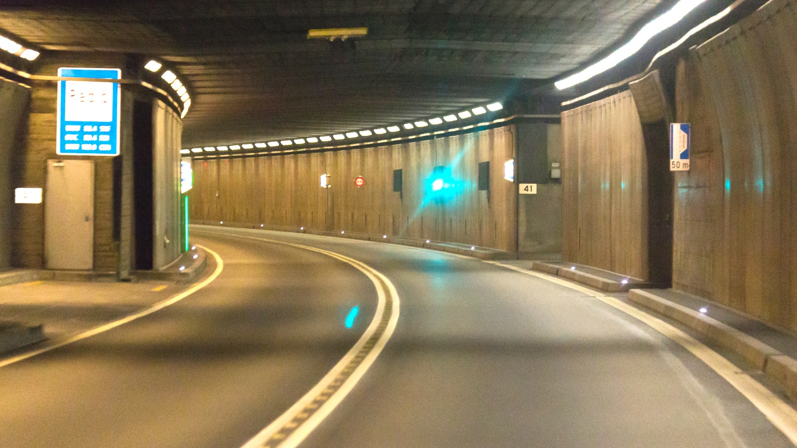 Interior of the Gotthard Road Tunnel showing the curved two-lane roadway, wall panels, and a radio frequency sign