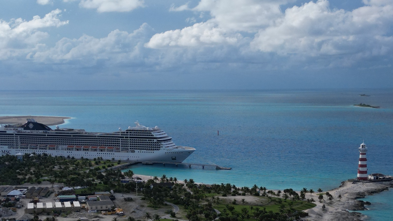 Aerial view of Ocean Cay MSC Marine Reserve in the Bahamas with an MSC ship at the pier, a red and white lighthouse, and a small neighboring cay in the distance