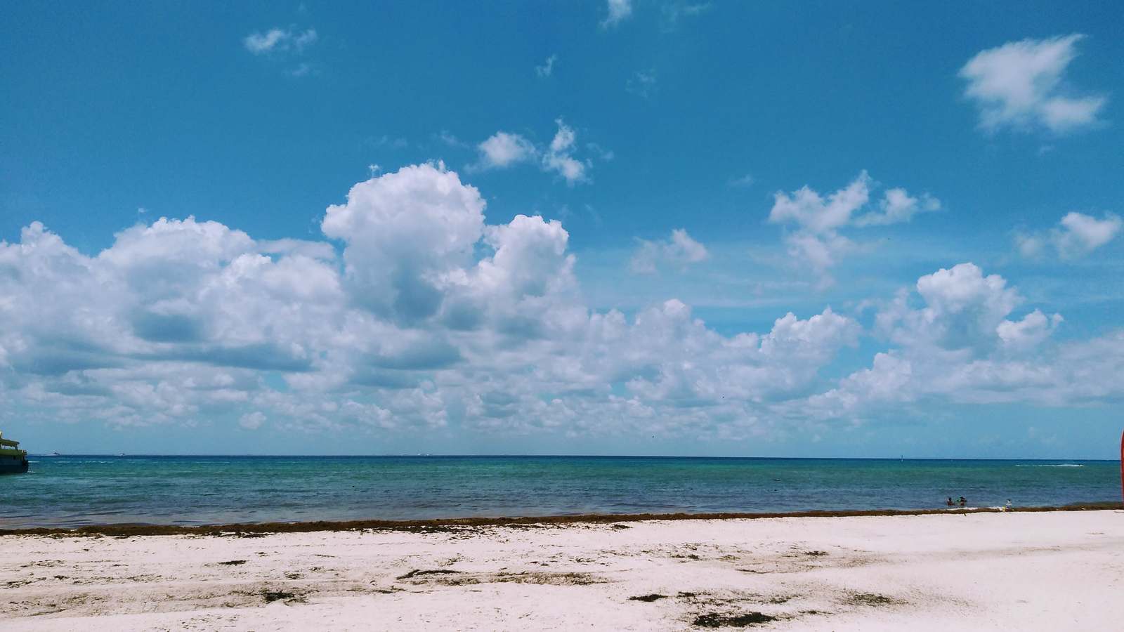 The white sand beach at Playacar in Playa del Carmen, Mexico, facing the turquoise Caribbean Sea under a blue sky with scattered clouds.