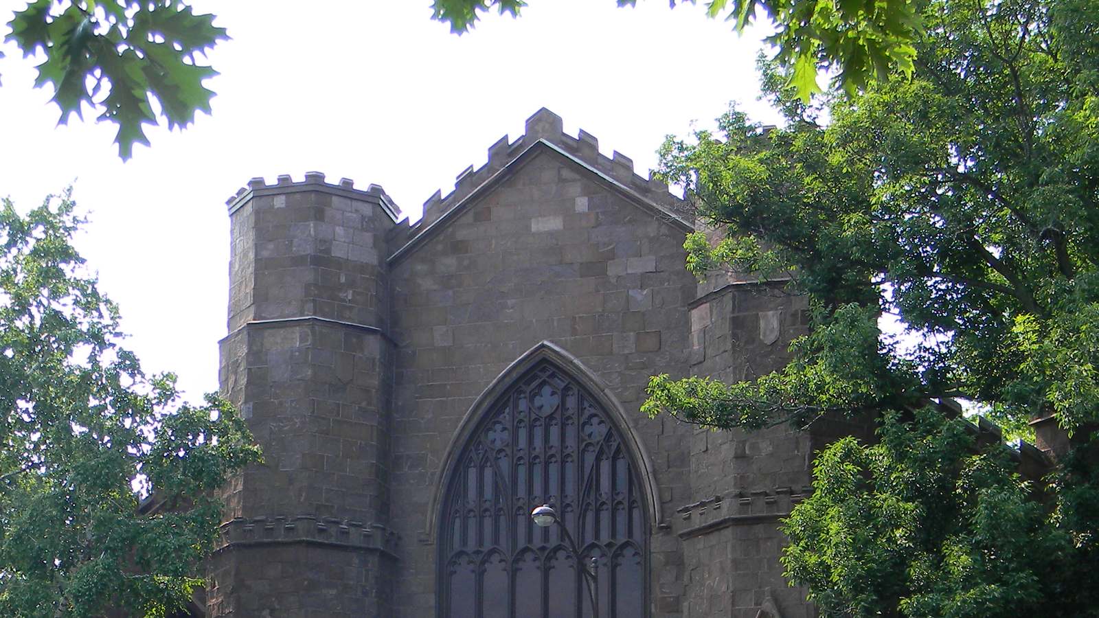 Stone Gothic facade of the Salem Witch Museum with a large arched window, framed by summer trees in Salem, Massachusetts.