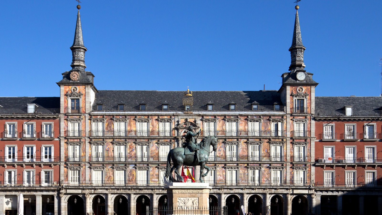 Plaza Mayor in Madrid with the equestrian statue in front of the painted Casa de la Panaderia facade under a clear blue sky