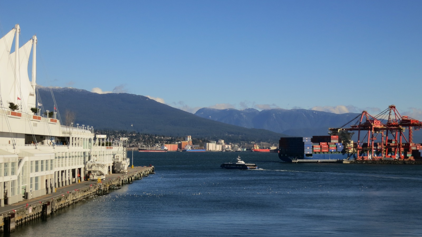 A SeaBus crossing Burrard Inlet beside Canada Place and the Port of Vancouver under a clear sky