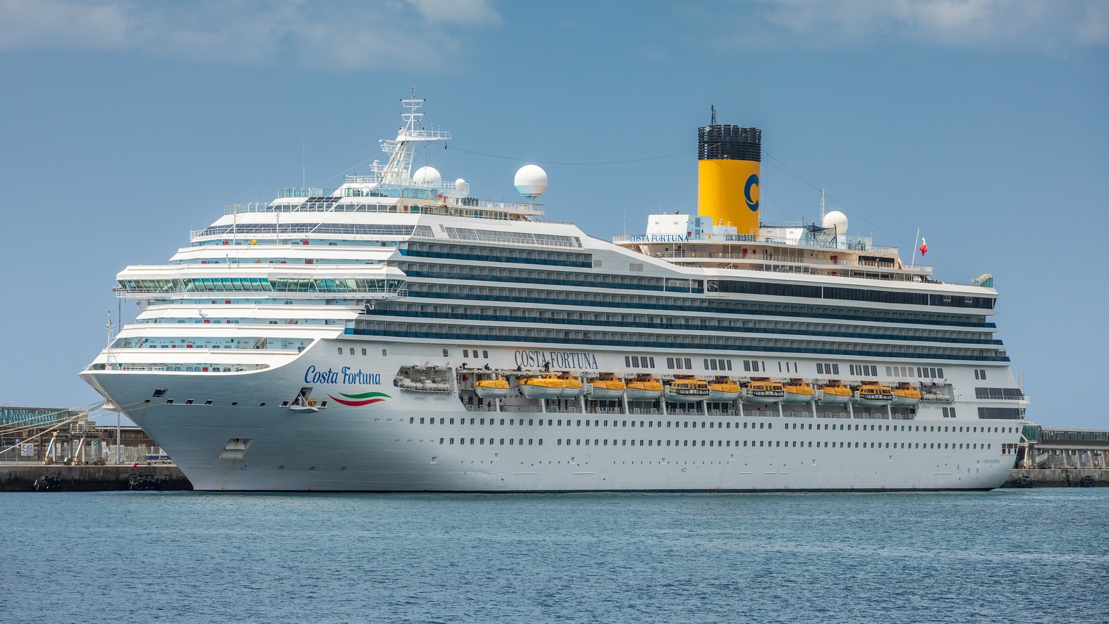 The cruise ship Costa Fortuna berthed at the Port of Funchal in Madeira, with the Costa Fortuna name on the bow and hull and the yellow Costa funnel amidships