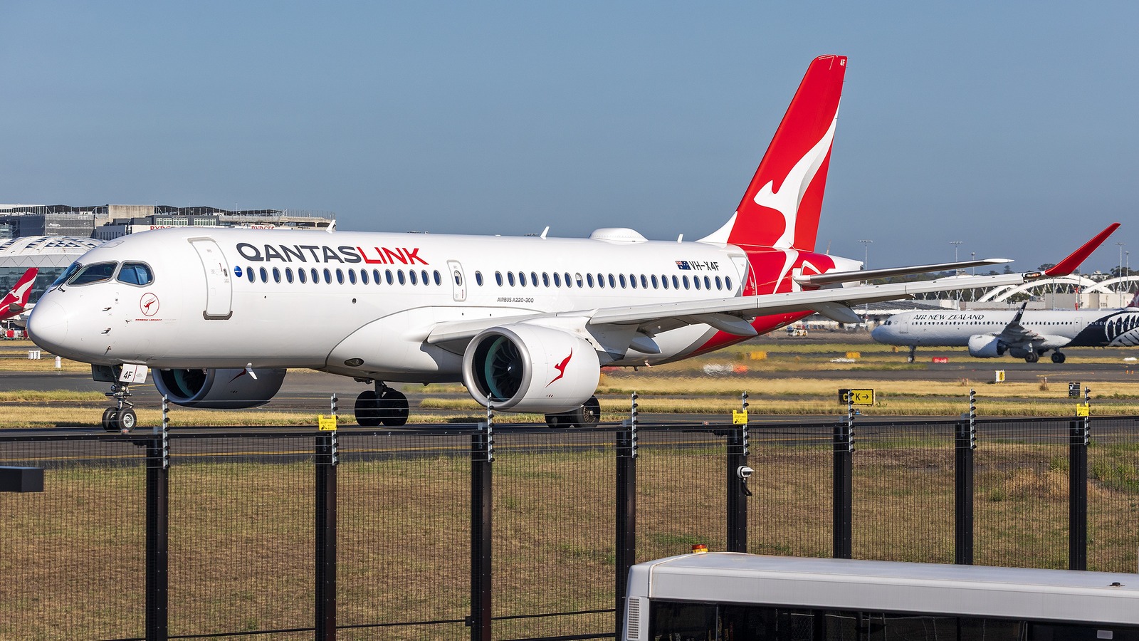 A QantasLink Airbus A220-300, registration VH-X4F, taxiing at Sydney Airport with the QantasLink titles, the Airbus A220-300 fuselage marking and the red flying kangaroo tail visible.