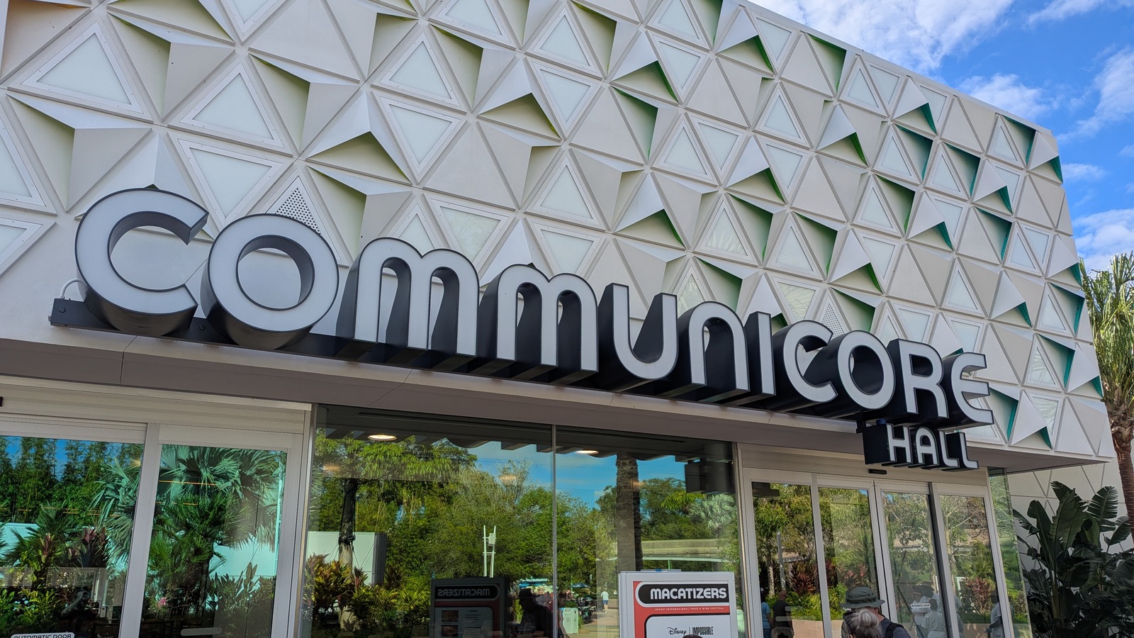 The entrance to CommuniCore Hall at EPCOT in Walt Disney World, with the hall name on the facade and guests at the glass doors.