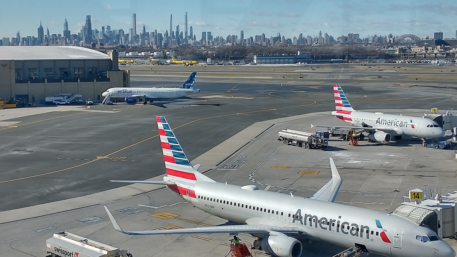 Airliners on the tarmac at LaGuardia Airport in Queens, New York, with the Manhattan skyline and Hell Gate Bridge beyond the airfield.