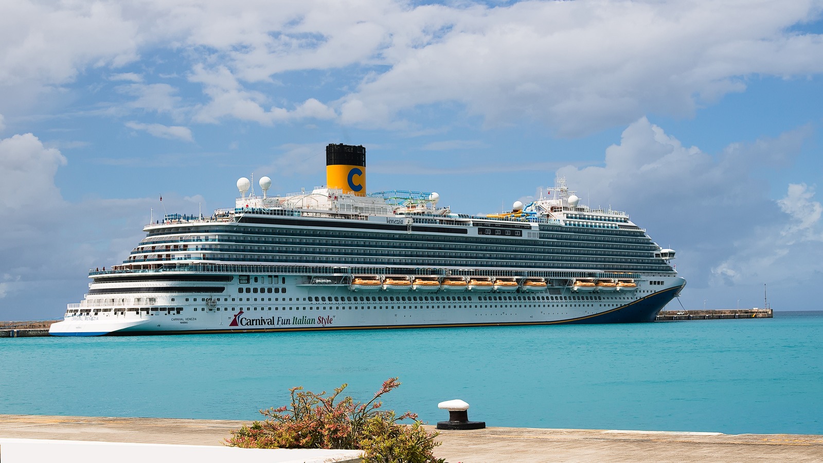 Carnival Venezia cruise ship at a sunny dock, yellow funnel with a blue C and Carnival Fun Italian Style marking on the hull
