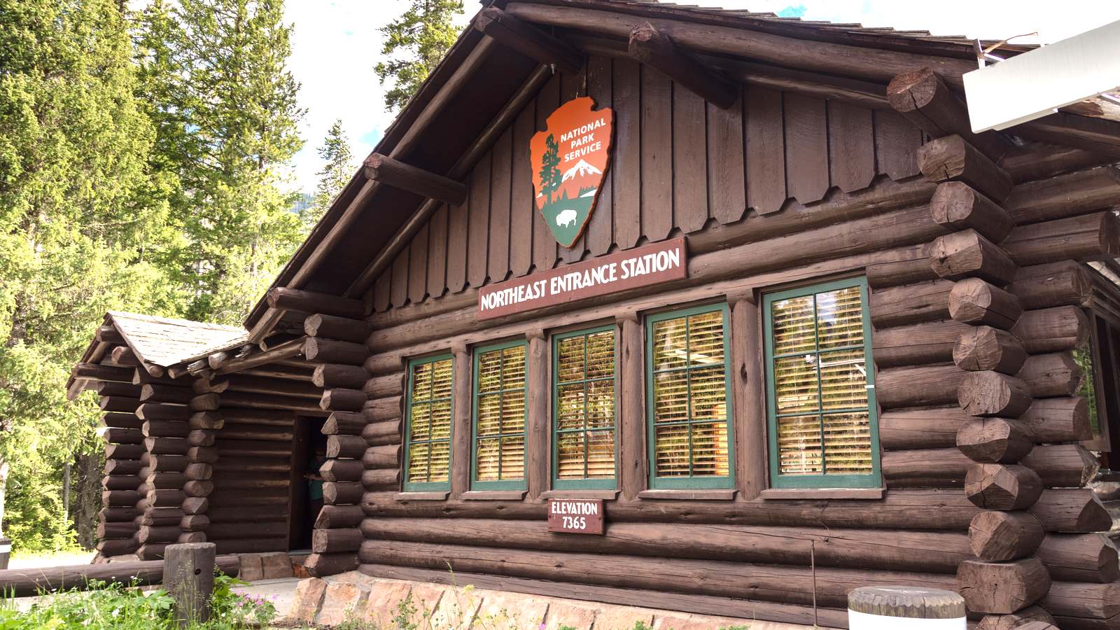 The log built Northeast Entrance Station at Yellowstone National Park, with the National Park Service arrowhead and an elevation 7365 sign on its wall.