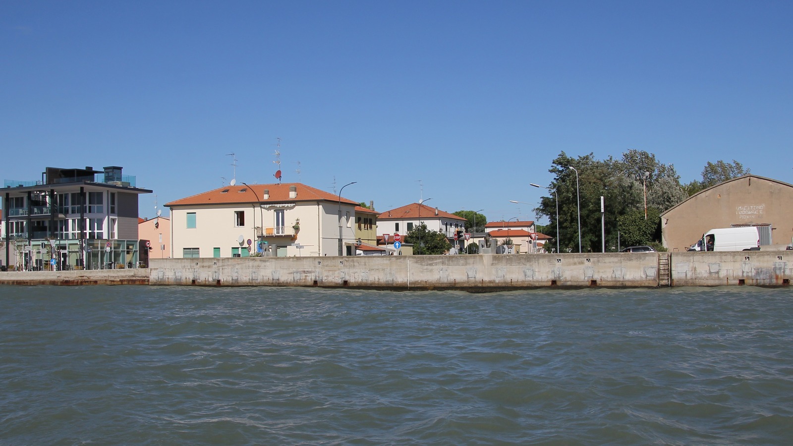 The Porto Corsini waterfront at Ravenna seen from the water, with the quay wall, houses and street furniture along the channel the ferry crosses