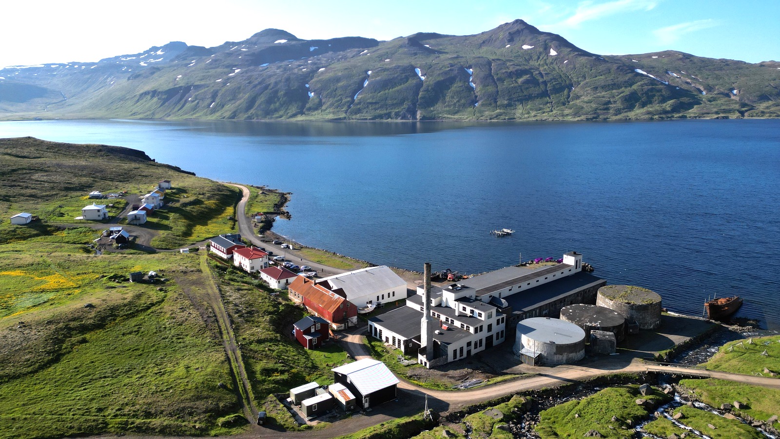 Aerial view of Djúpavík on Iceland's Strandir coast in summer, with the old herring factory, the gravel coast road and the fjord.