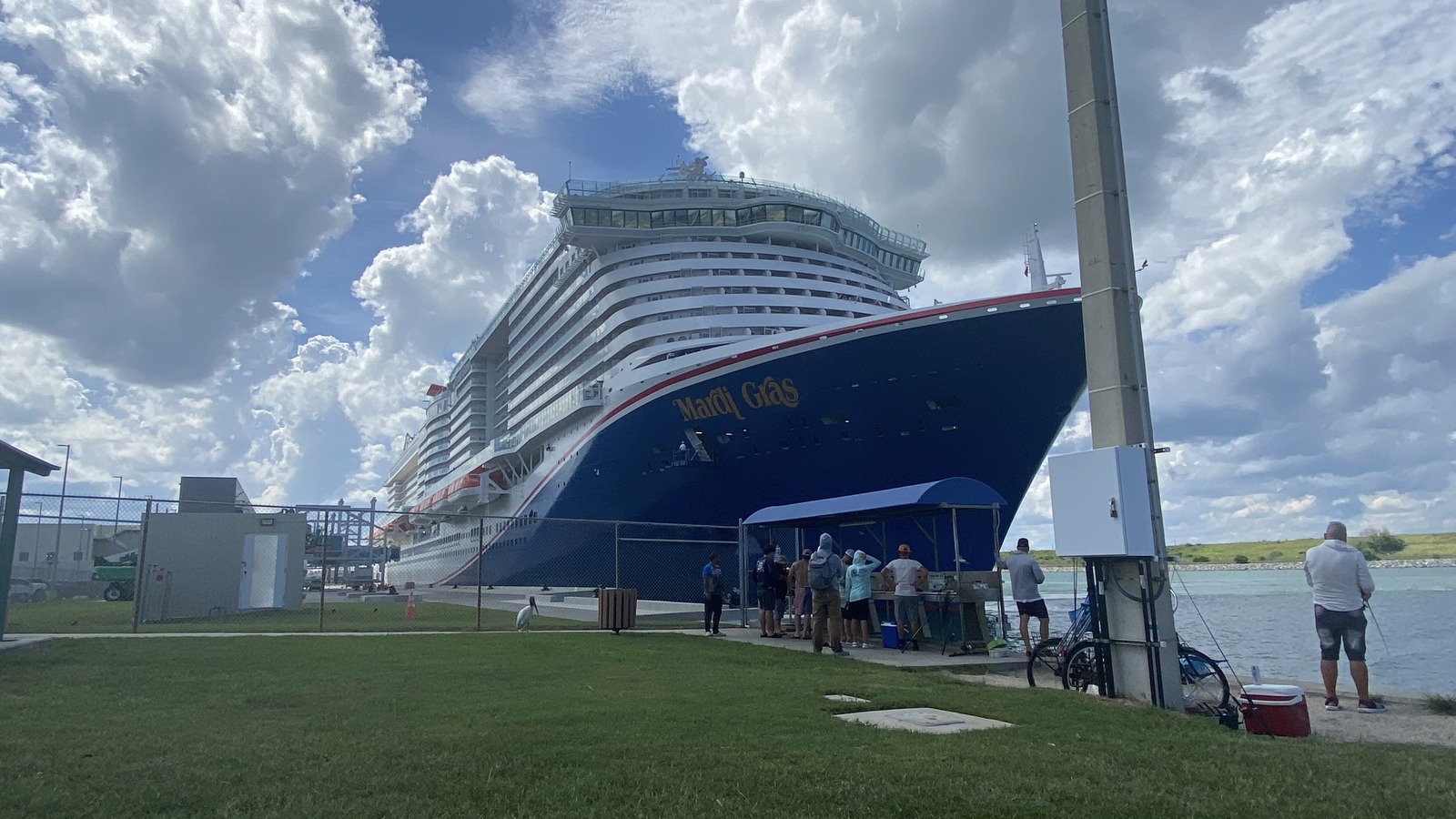 The Carnival Mardi Gras cruise ship docked at Port Canaveral, Florida, on September 5, 2026, with its dark blue hull and white superstructure seen from the shore under a cloudy sky.