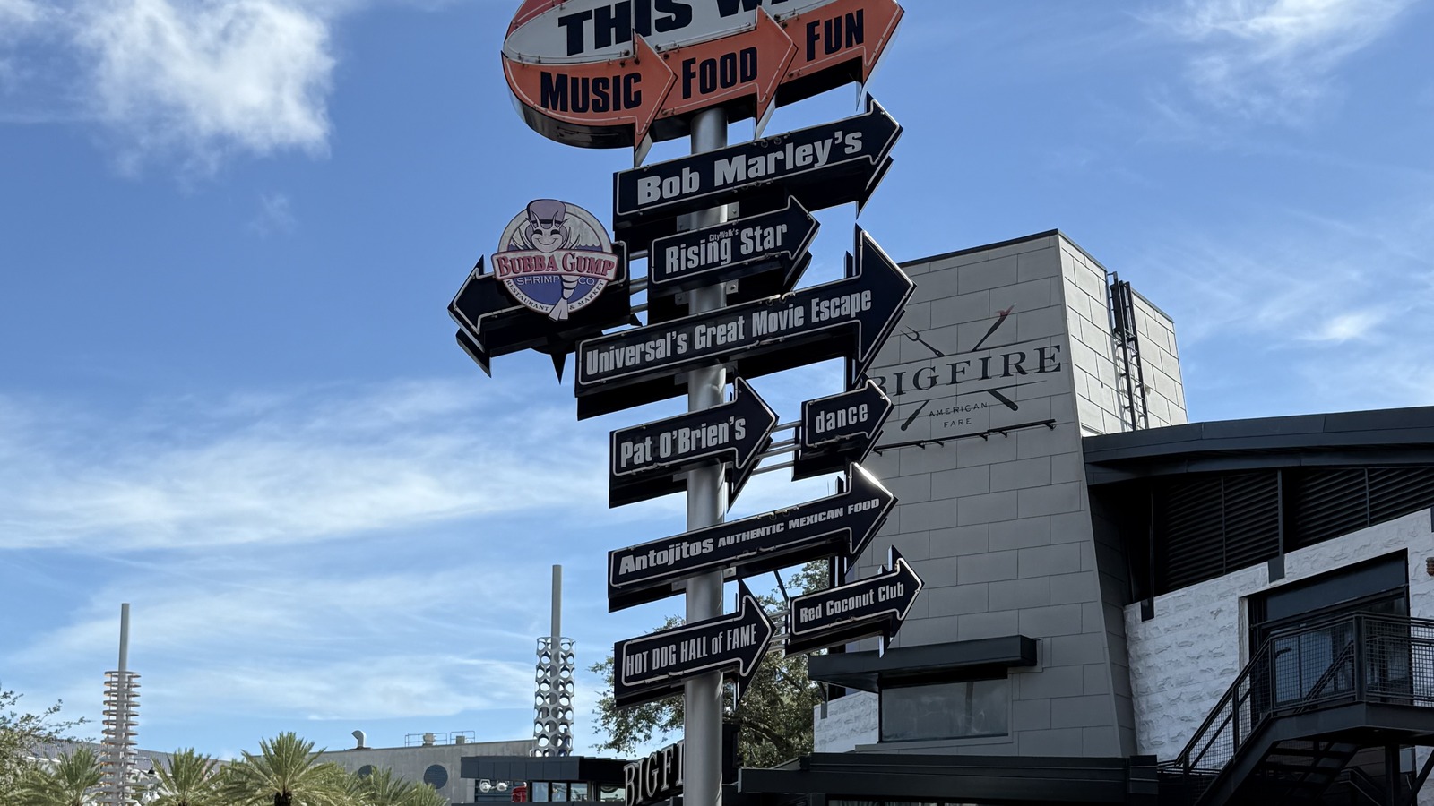Directional sign at Universal CityWalk in Orlando naming Universal's Great Movie Escape, Bob Marley's, and other venues under a blue sky.