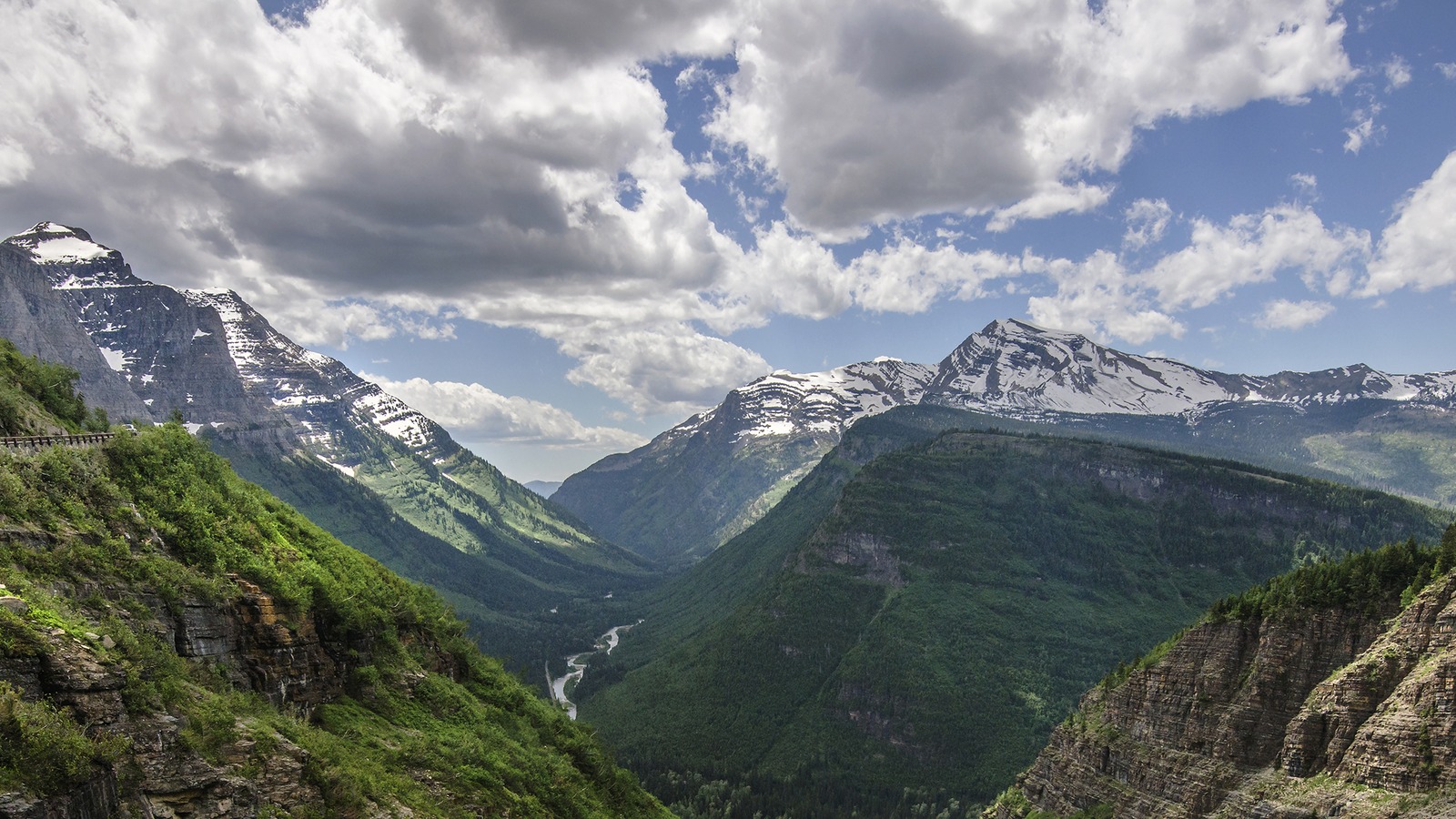 Going-to-the-Sun Road clinging to a cliff above a waterfall and green valley in Glacier National Park