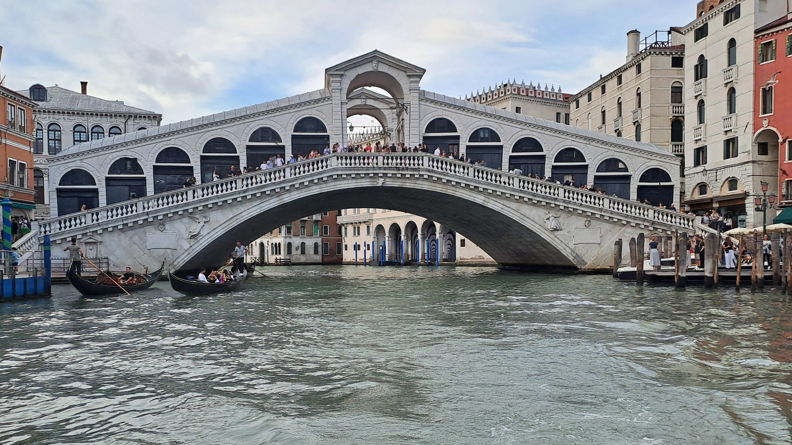 Rialto Bridge spanning the Grand Canal in Venice with gondolas passing below and crowds on the bridge