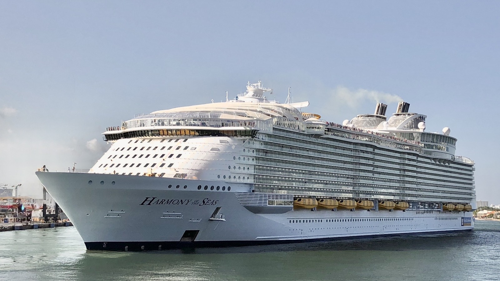 Harmony of the Seas cruise ship in port, bow name visible, photographed from the water under a clear sky