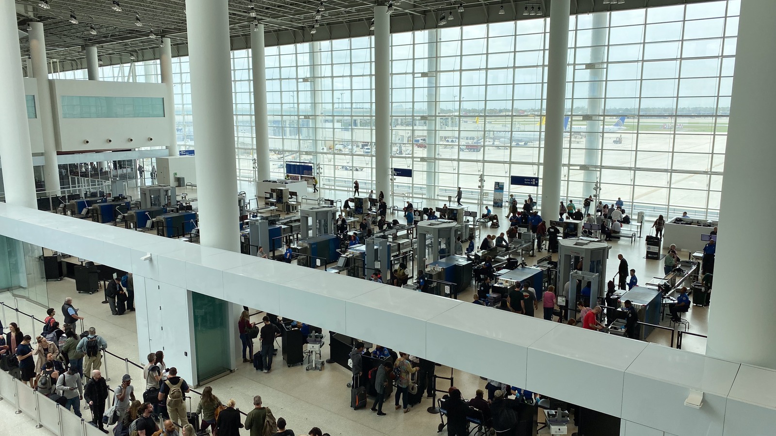 Travelers queue at TSA screening lanes inside a bright United States airport terminal