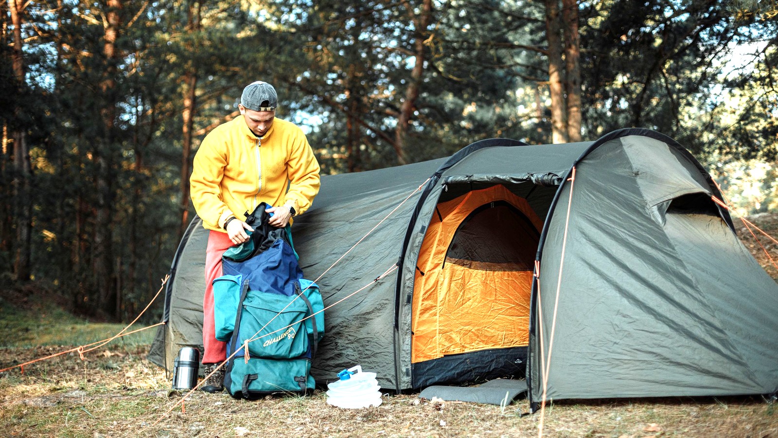 A camper organizing gear beside a pitched tent in a forest.