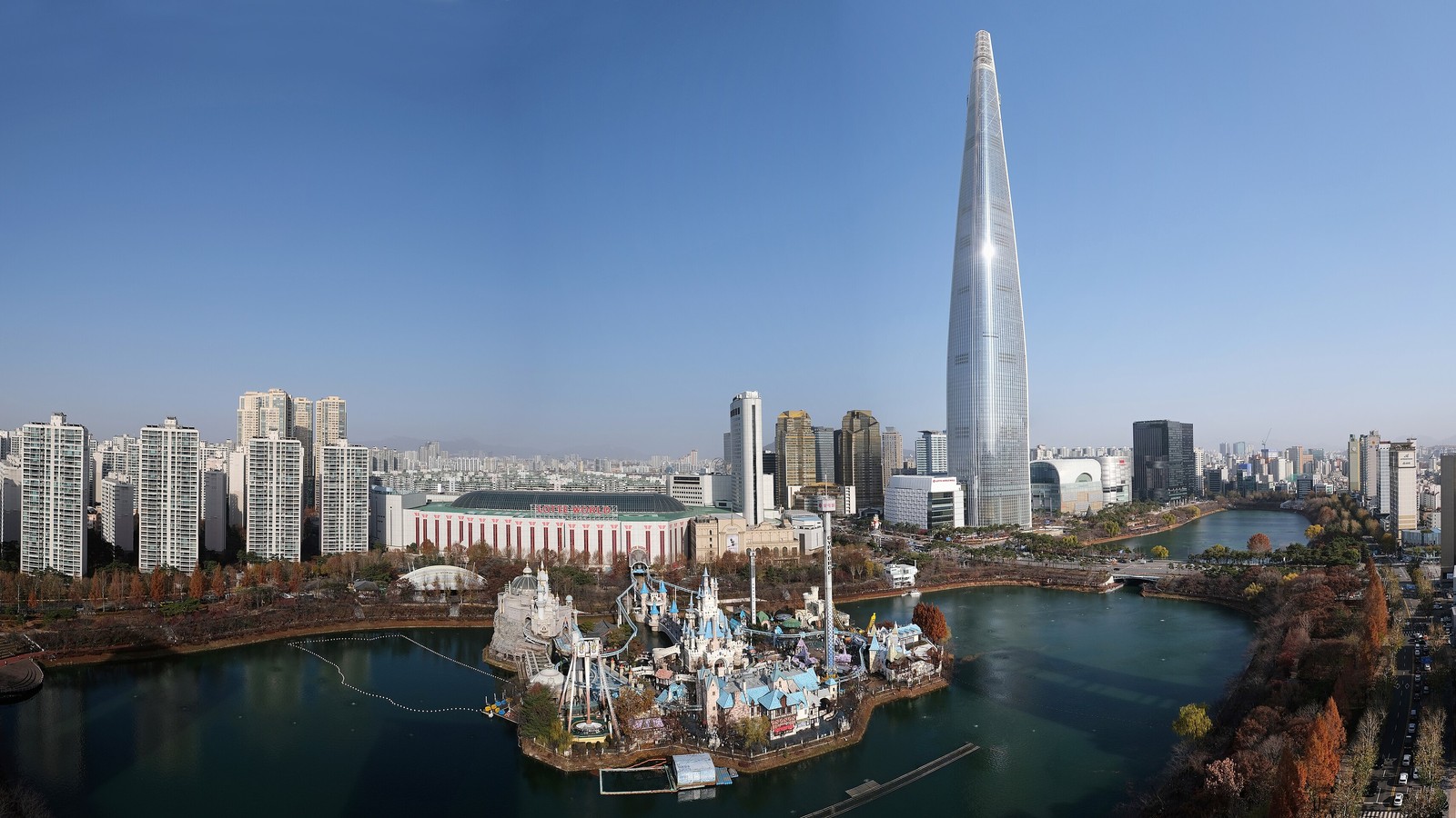 Wide aerial view of indoor Lotte World Adventure beside Magic Island and Seokchon Lake