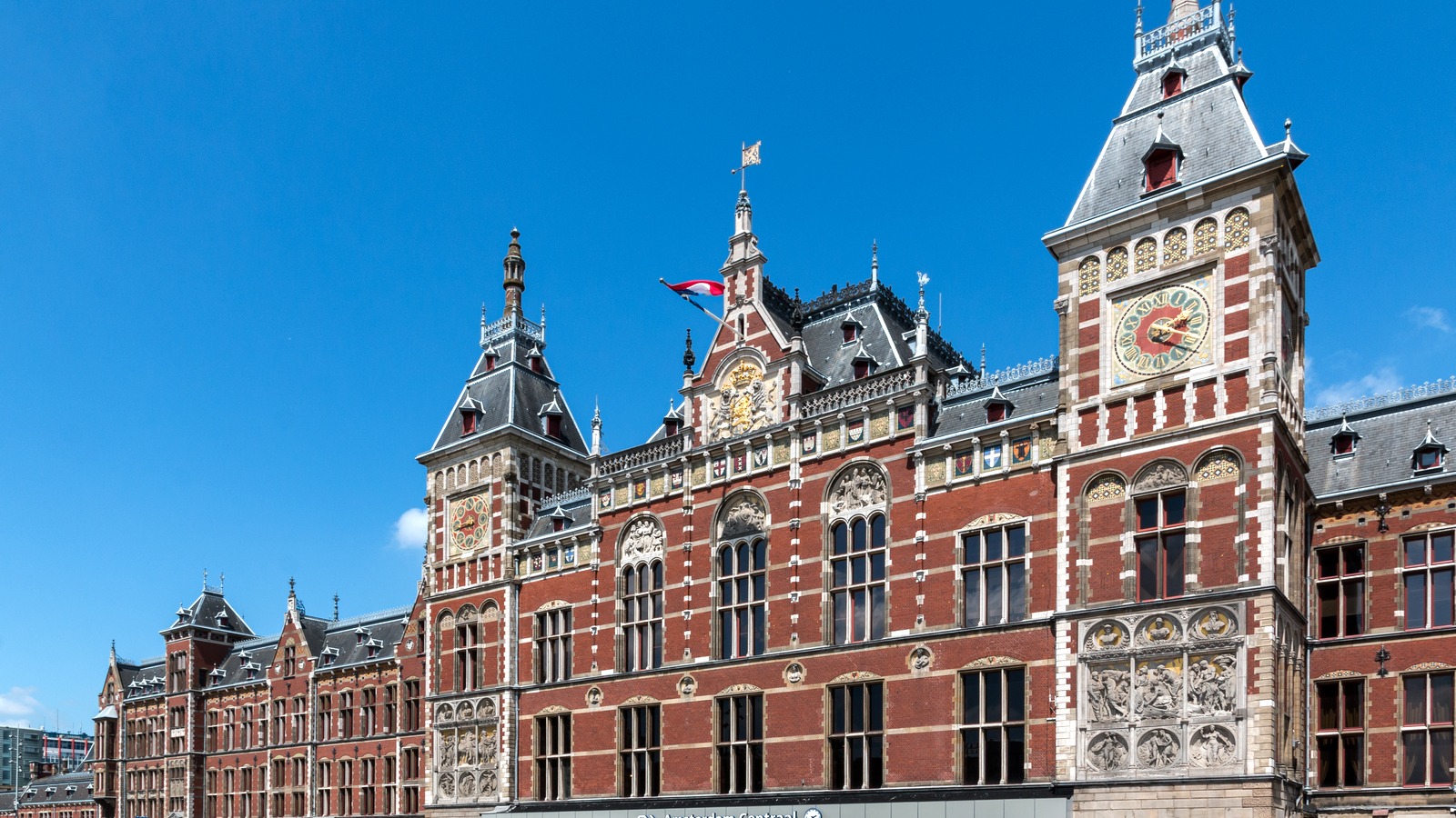 Amsterdam Centraal station brick facade and clock tower under a clear blue sky