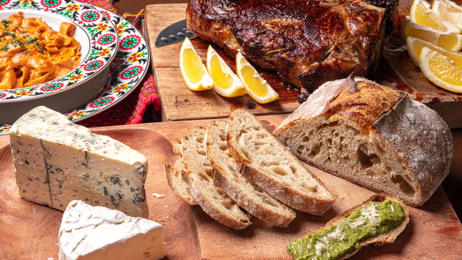 Florentine steak with pasta, bread, pesto, and cheese on a rustic table