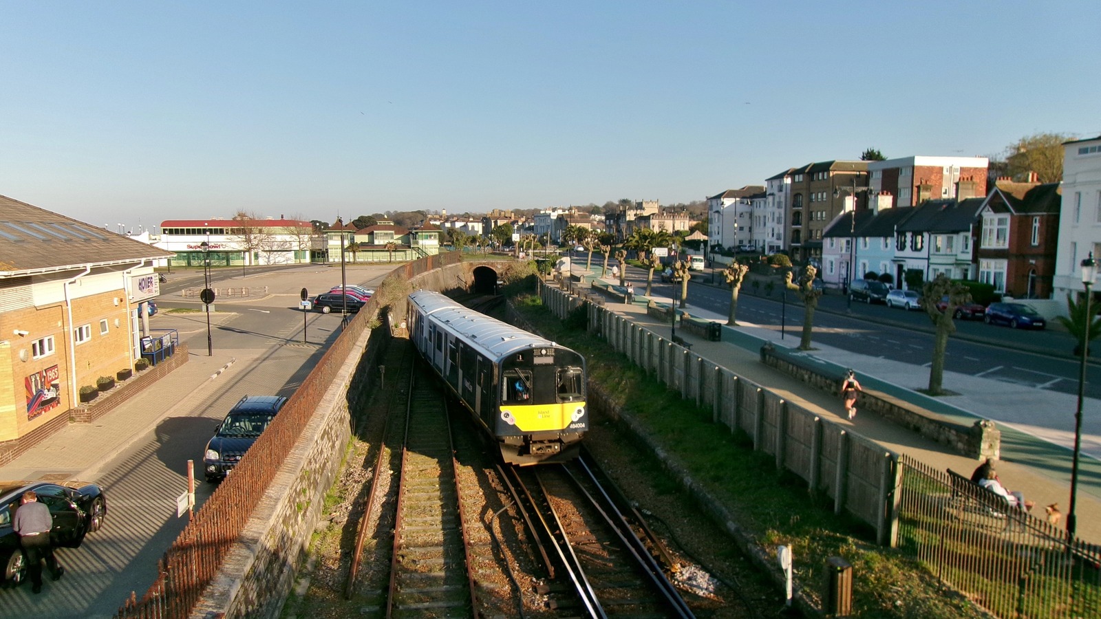 An Island Line Class 484 train in the cutting at Ryde Esplanade on the Isle of Wight, with the seafront town behind it.