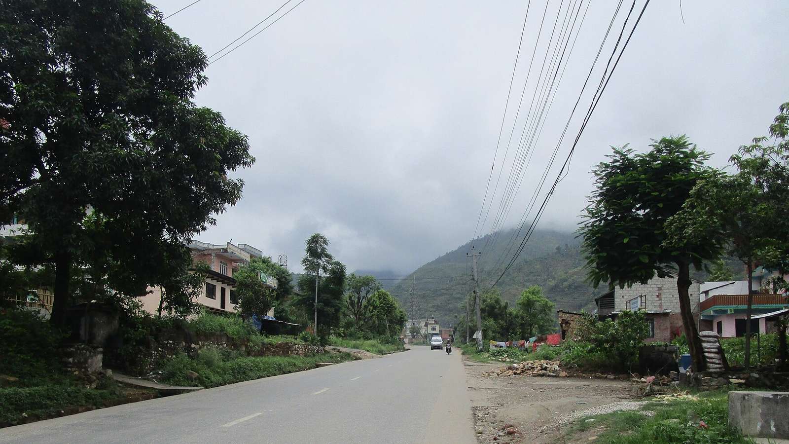 File photo of the Prithvi Highway at Malekhu in Dhading, Nepal, taken in 2016, a paved road running between roadside houses toward a cloud-covered hillside