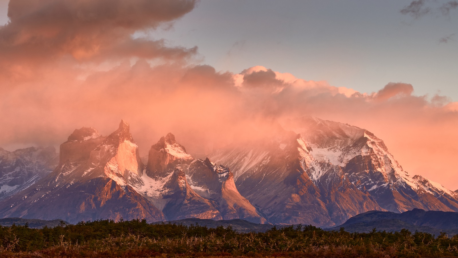 Snow dusted Cuernos del Paine massif glowing at sunset above dark forest in Torres del Paine National Park