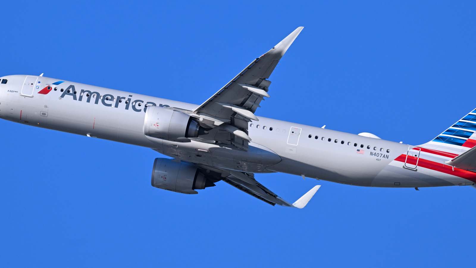 An American Airlines Airbus A321neo climbs against a clear blue sky after takeoff.