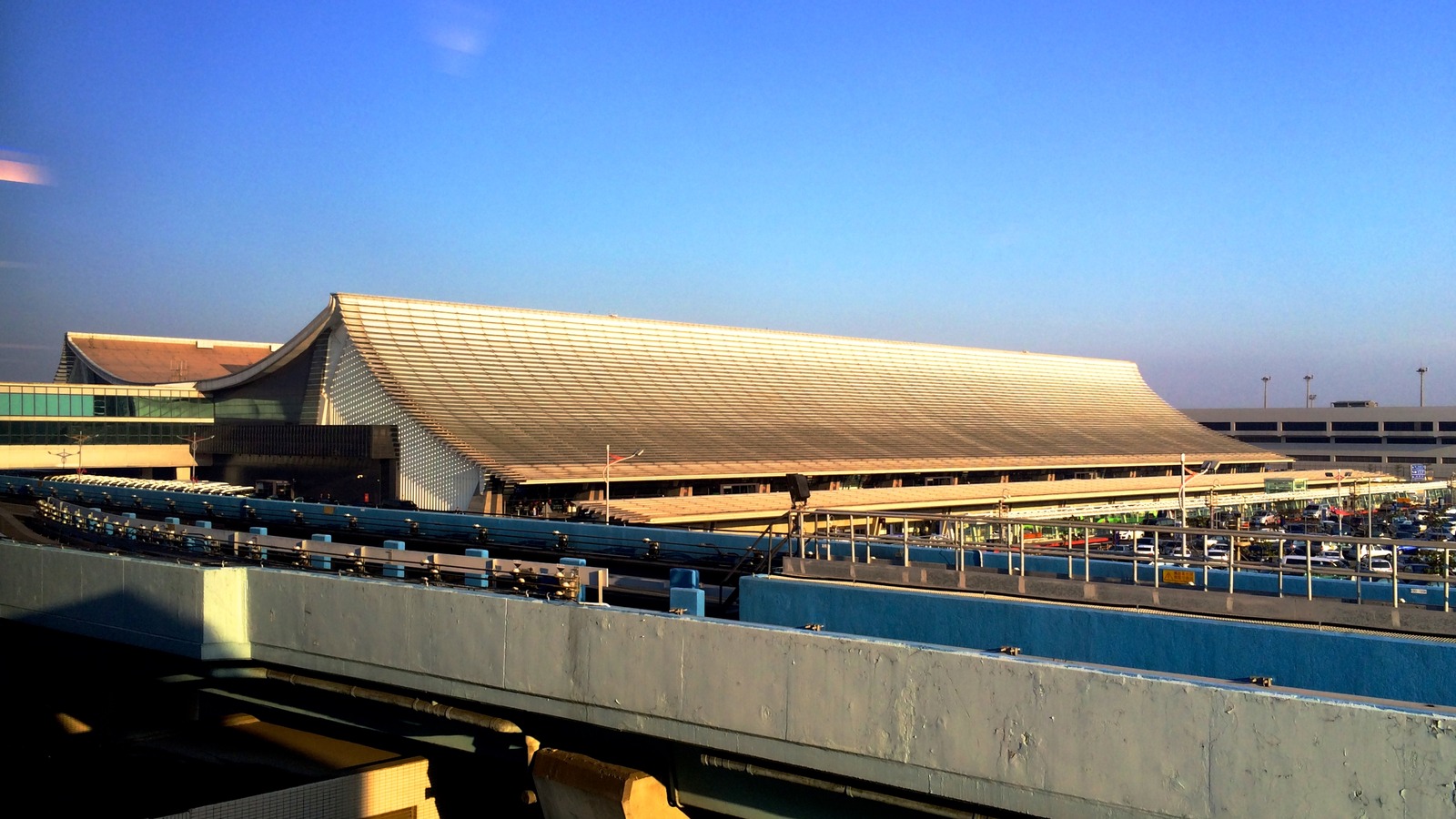 Exterior of Terminal 1 at Taiwan Taoyuan International Airport, with the curved metal roof and elevated roadway in daylight.