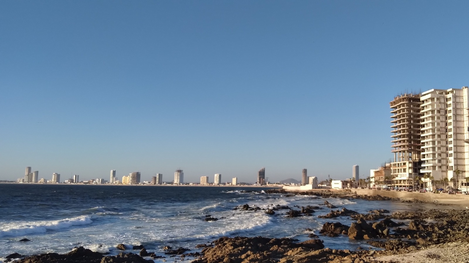 Rocky Mazatlán seawall coast with surf and the city skyline under a clear sky, in a March 2025 file photo