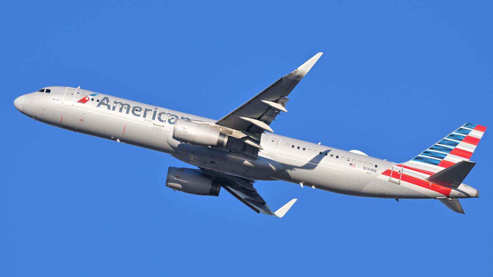 An American Airlines Airbus A321 climbs against a clear blue sky after takeoff.