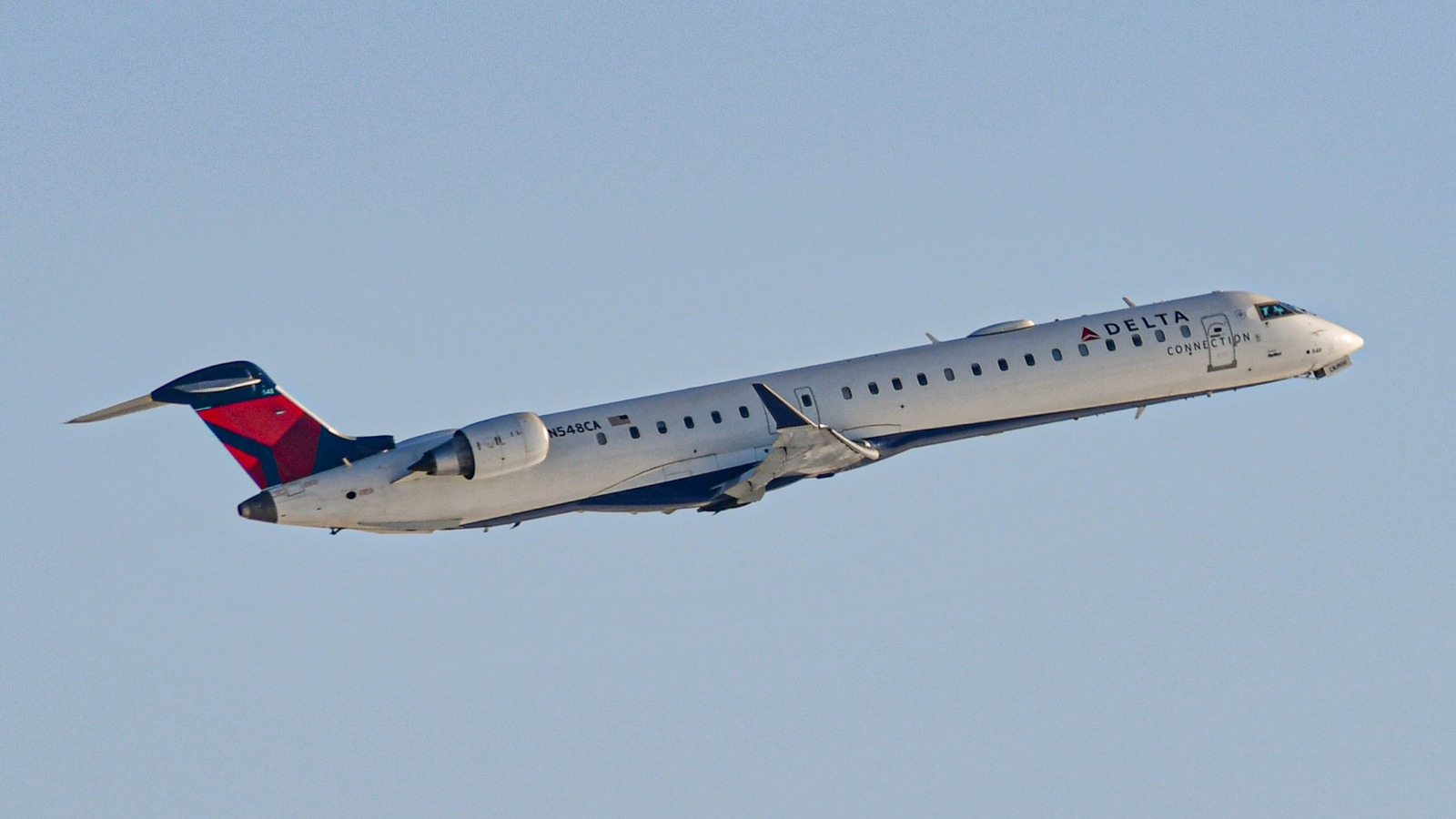 A Delta Connection Bombardier CRJ-900 regional jet climbing after takeoff against a clear blue sky.