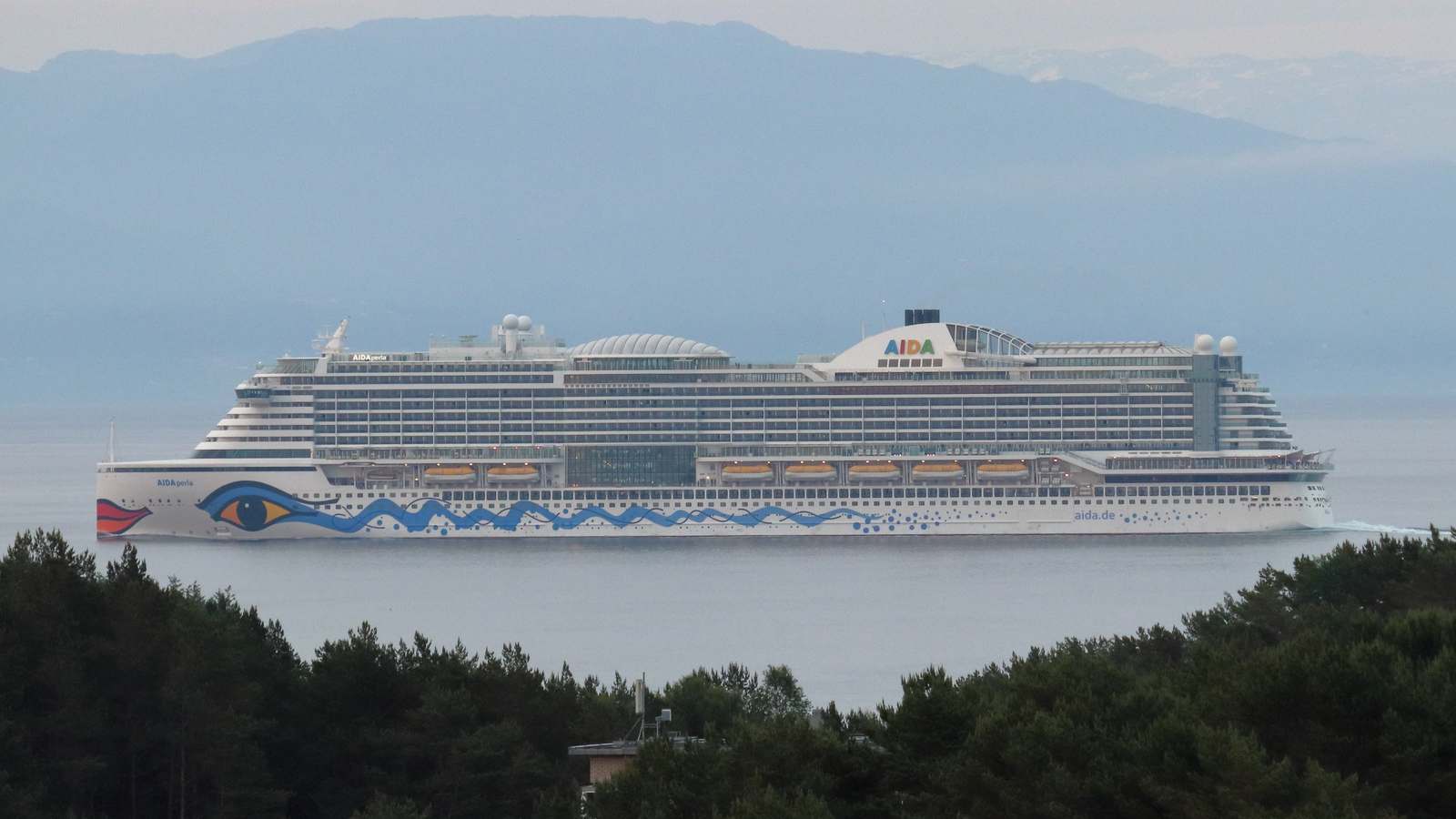 Cruise ship AIDAperla sailing through Bjornafjorden in Norway with mountains behind
