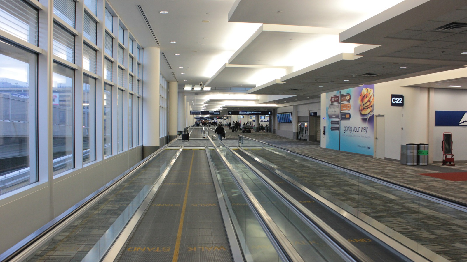 A bright, quiet concourse at Minneapolis-St. Paul International Airport with moving walkways beside tall windows and gate C22 signage.