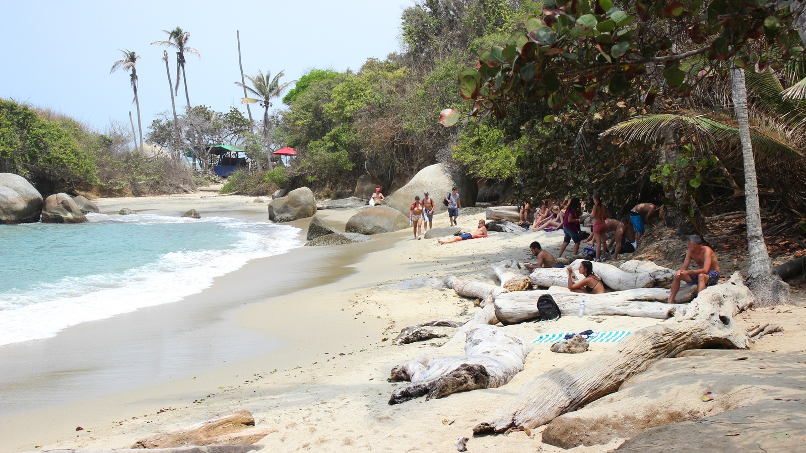 Visitors on Cabo San Juan beach in Tayrona National Park, Colombia, with turquoise water, sand, and forested boulders