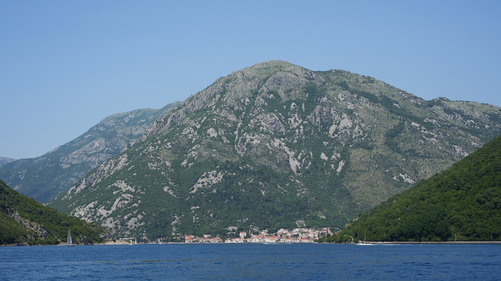 The Bay of Kotor in Montenegro seen from the water with mountains behind a small waterfront town, photographed June 2025