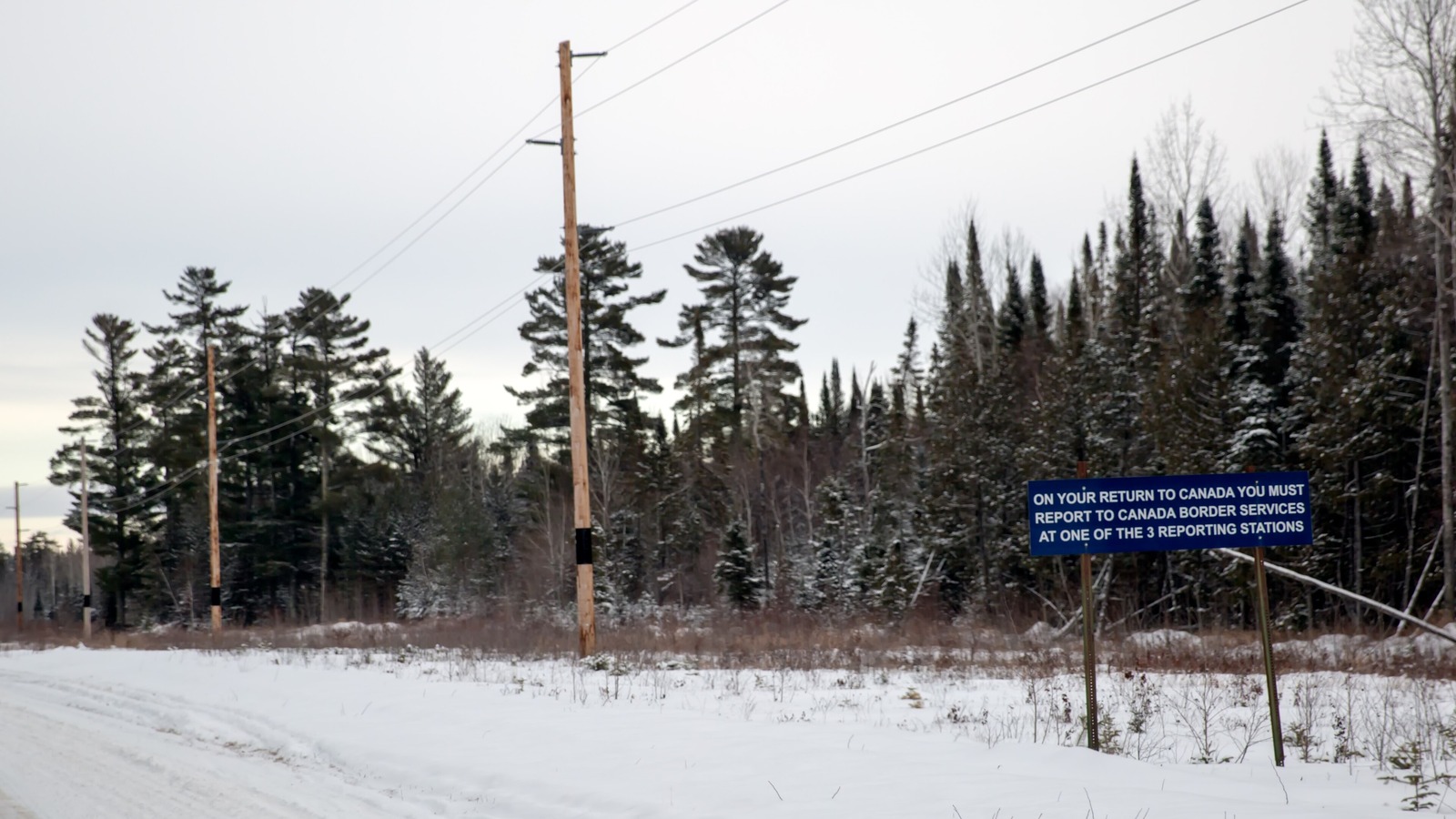 Blue sign near a snowy road at the Northwest Angle, Minnesota, telling travelers to report to Canada Border Services at a reporting station